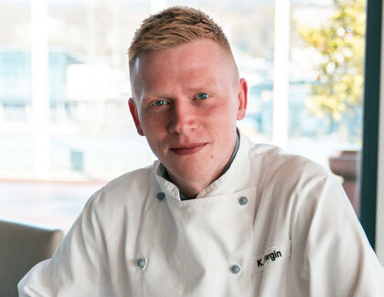 Kevin Wergin sitzt mit einem Kaffee am Tisch. Mit auf dem Tisch steht eine Blume.