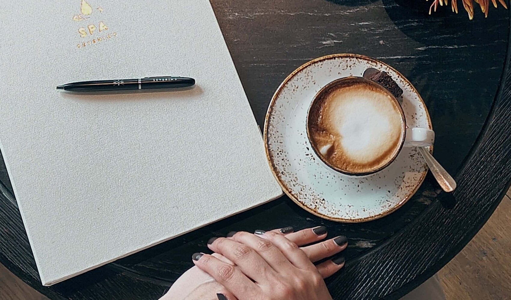 Blick von oben auf Jana Hohlfeld, die mit einem Kaffee und eine Mappe an einem Tisch sitzt.