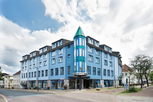 ATLANTIC Hotel Vegesack Außenansicht Eine Außenansicht vom ATLANTIC Hotel Vegesack. Die Außenfassade ist blau und das Hotel hat vier Stockwerke. Vor dem Hotel stehen drei Blumentöpfe und an der linken Seite ist ein Schild mit der Aufschrift "Garage Einfahrt". Über dem Eingang steht "ATLANTIC Hotel".