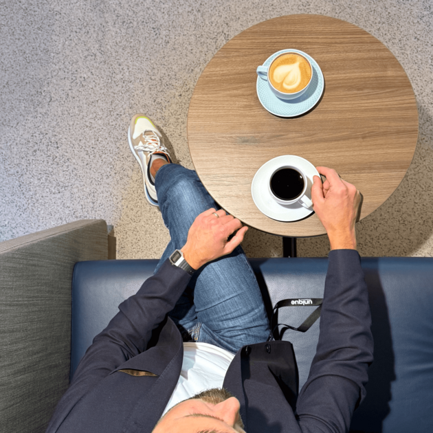Blick von oben auf Frederik Schönke, der mit einem schwarzen Kaffee und einem Cappuccino an einem Tisch sitzt.