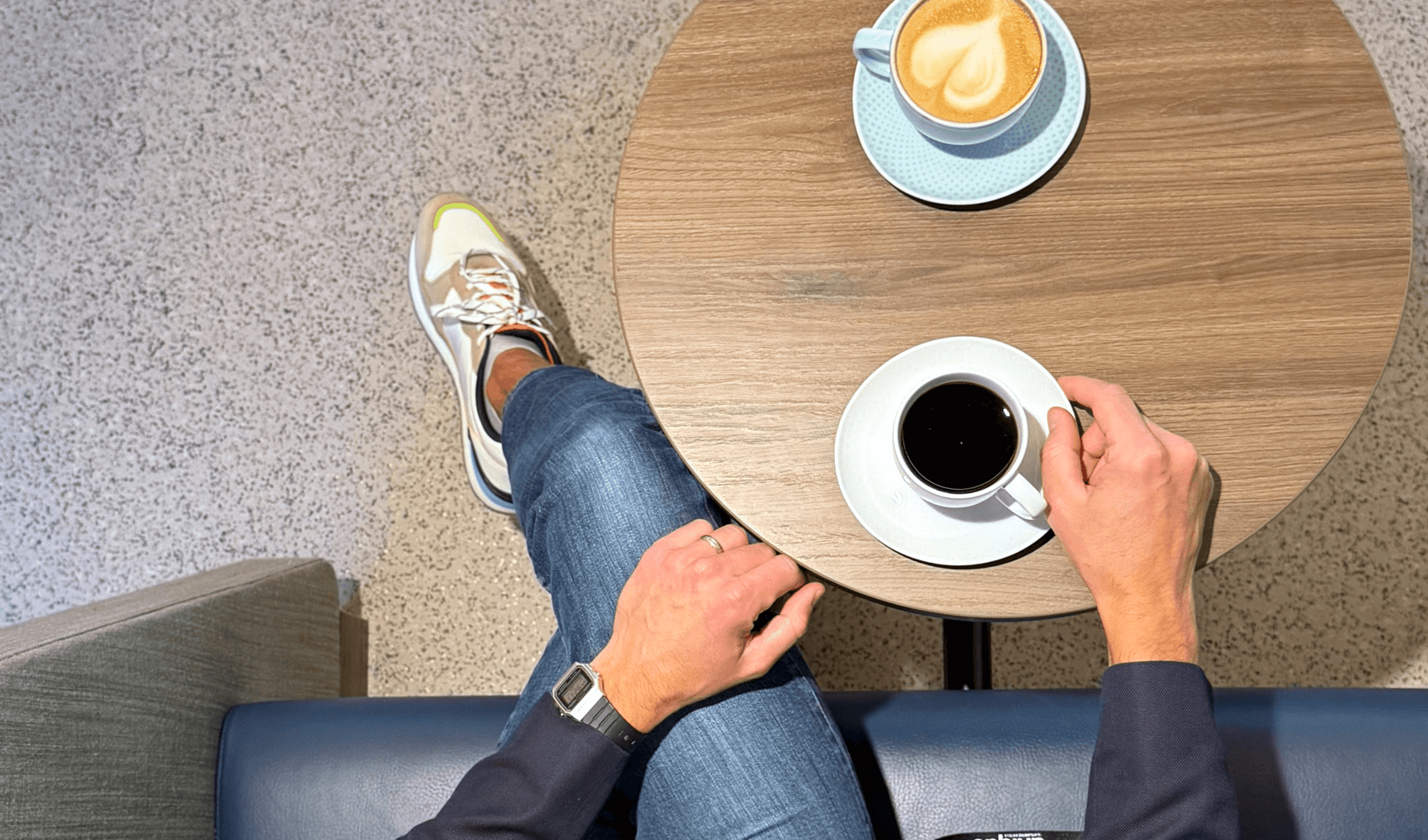 Blick von oben auf Frederik Schönke, der mit einem schwarzen Kaffee und einem Cappuccino an einem Tisch sitzt.