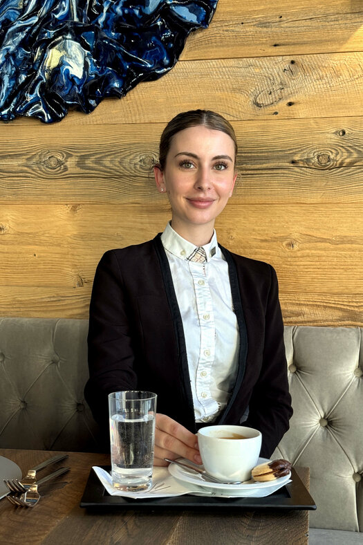 Nadja Karrer (Restaurant Supervisor, Severin*s – The Alpine Retreat) sitzt an einem Tisch mit einer Tasse Kaffee