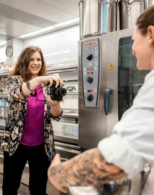 Viktoria Rathjen stands in the hotel kitchen with a camera in her hand and photographs a chef