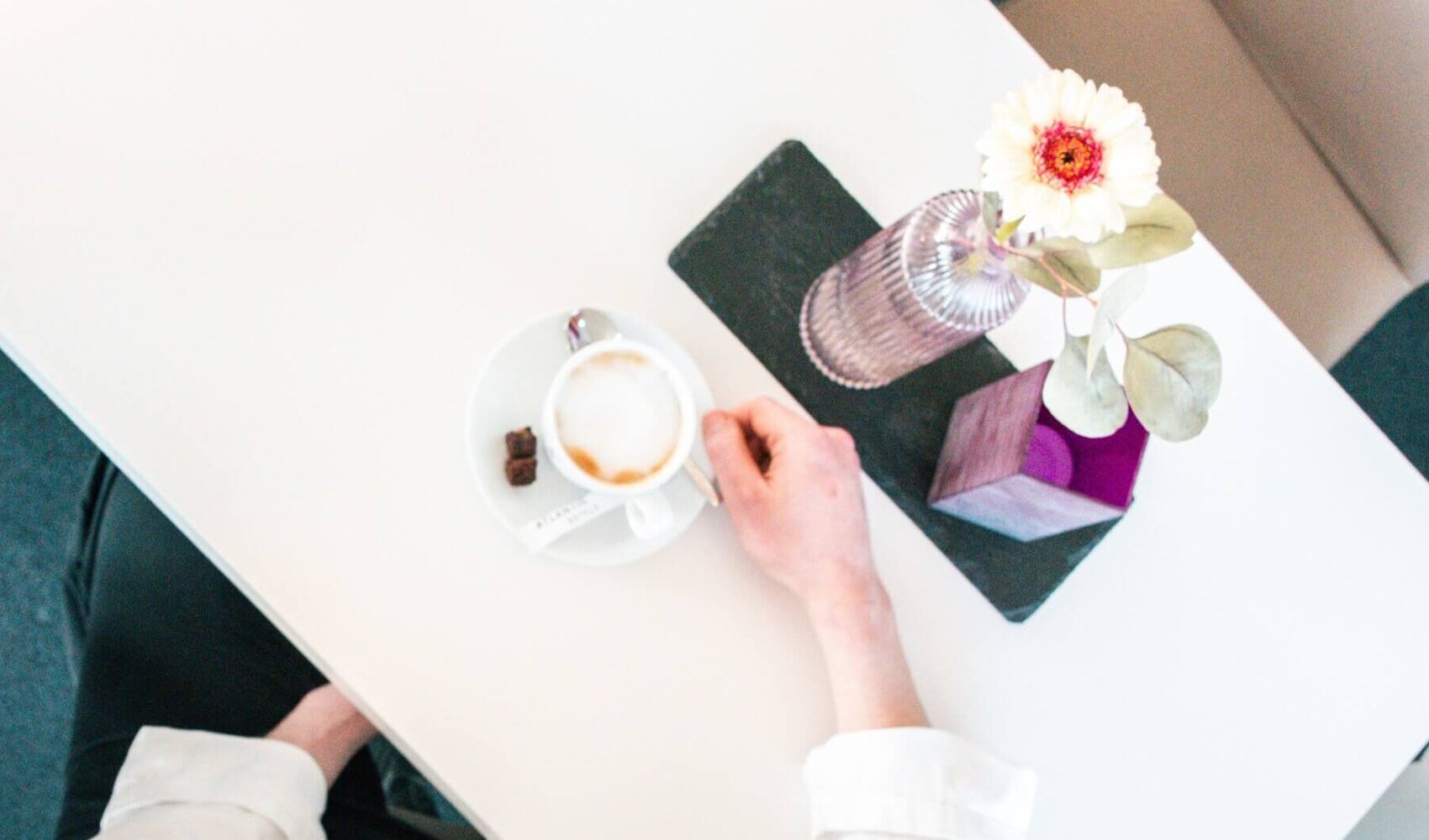 Kevin Wergin ist von oben am Tisch sitzend zu sehen. Es stehen ein Kaffee und Blumen auf dem Tisch.