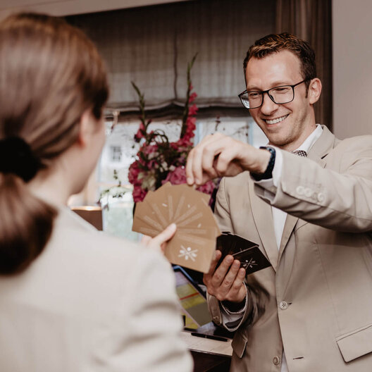 Team-Moment: Mitarbeitende des Severin*s Resort & Spa beim Kartenspiel Eine Mitarbeiterin und ein Mitarbeiter in beigen Anzügen spielen Karten.