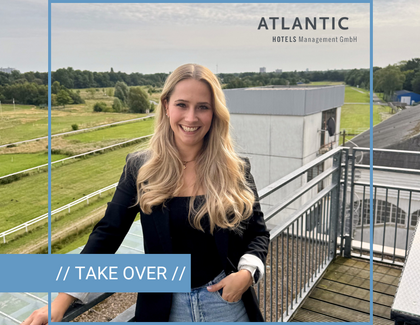 Eine Frau steht lächelnd auf einem Balkon. Sie trägt eine blaue Hose, einen schwarzen Blazer und eine schwarzes Oberteil. Oben rechts in der Ecke ist das Logo der ATANTIC Hotels Management GmbH abgebildet und unten links ist ein hellblauer Streifen mit der Aufschrift "// TAKE OVER //". Die Person ist umrahmt von hellblauen Linien, die zu einem Quadrat angeordnet sind. 