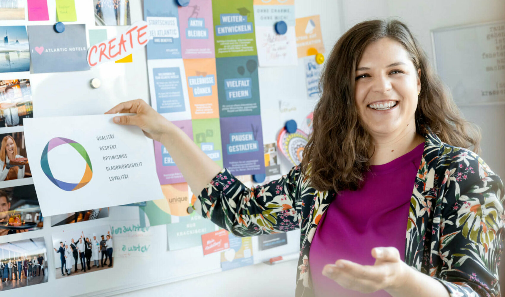 Viktoria Rathjen steht vor ihrem Kreativ-Whiteboard im Büro und hält einen Zettel mit den Unternehmenswerten hoch.