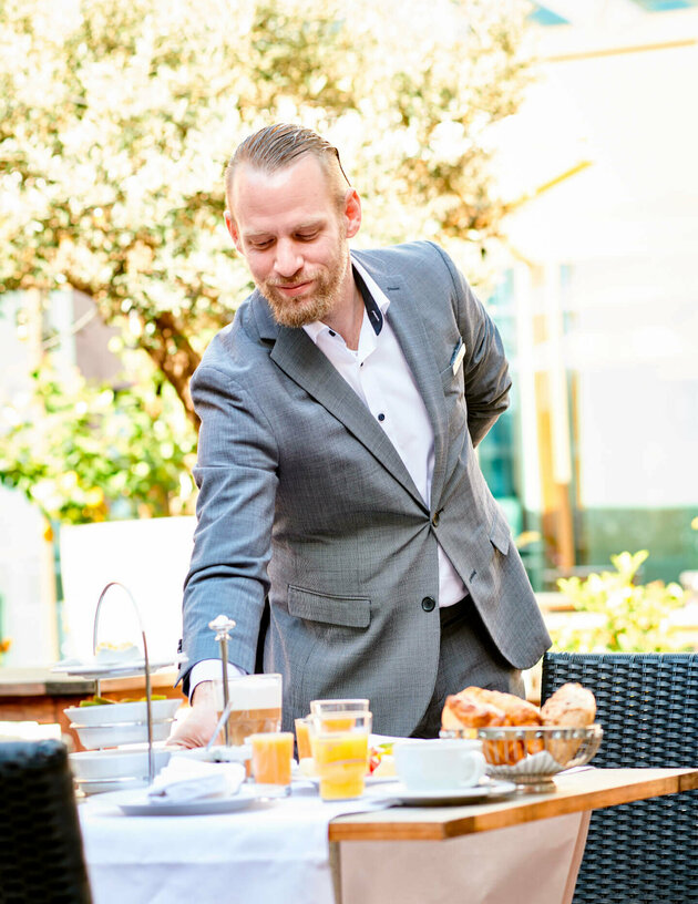 Tobias Wilhelm deckt auf der Terrasse den Frühstückstisch ein.