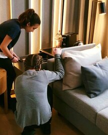 Zwei Mädchen befinden sich in einem Hotelzimmer. Sie machen eine Fehlersuche um zu gucken, ob das Zimmer richtig geputzt wurde.