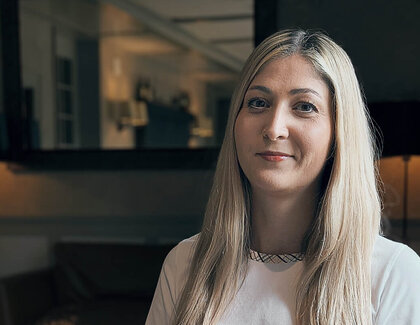 Jana Hohlfeld hat lange blonde Haare und sitzt mit einem Kaffee und einer Severin*s-Spa-Mappe am Tisch. 