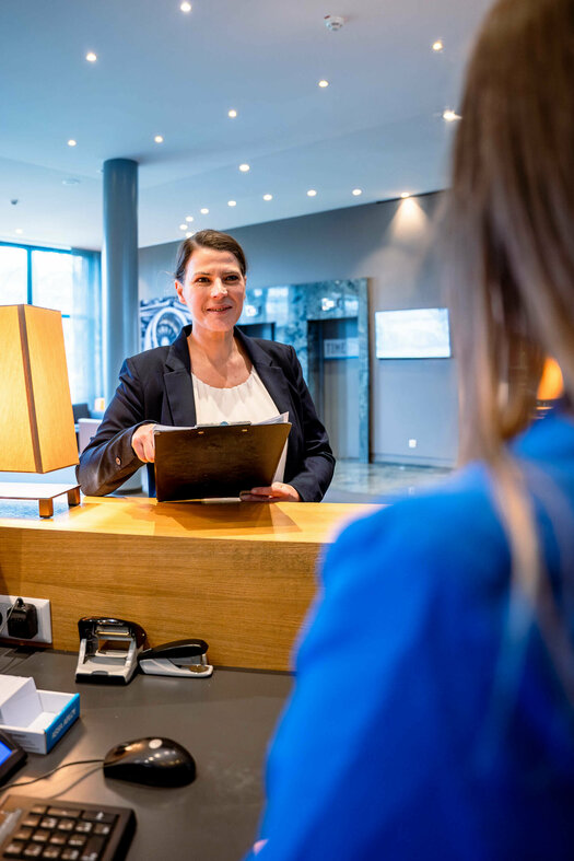 Hoteldirektorin steht am Tresen der Rezeption und spricht mit einer Mitarbeiterin