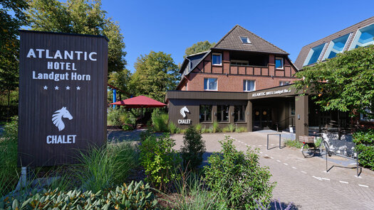 Außenansicht ATLANTIC Hotel Landgut Horn. Links ist ein Schild mit Logo und geradeaus ist das Hotel zu sehen. 