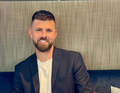 Frederik Schönke sitzt auf einer Bank an einem Tisch. Vor ihm steht ein schwarzer Kaffee und ein Cappuccino auf einem Tisch.