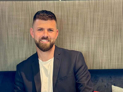 Frederik Schönke sitzt auf einer Bank an einem Tisch. Vor ihm steht ein schwarzer Kaffee und ein Cappuccino auf einem Tisch.