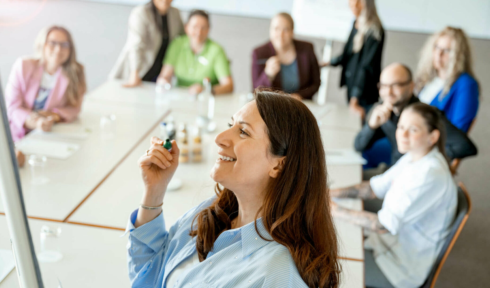 Eine Dame steht am Flipchart, im Hintergrund sitzen weitere Menschen am Tisch