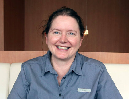 Die dunkelhaarige gastronomischen Leitung Gabriele Pioch sitzt im Restaurant an einem dunklen Tisch mit anthraziten Läufer und lächelt freudig in die Kamera. Auf dem Tisch stehen zwei Cappuccini sowie zwei Brownies auf einen weißen Teller und eine grüne Pflanze.