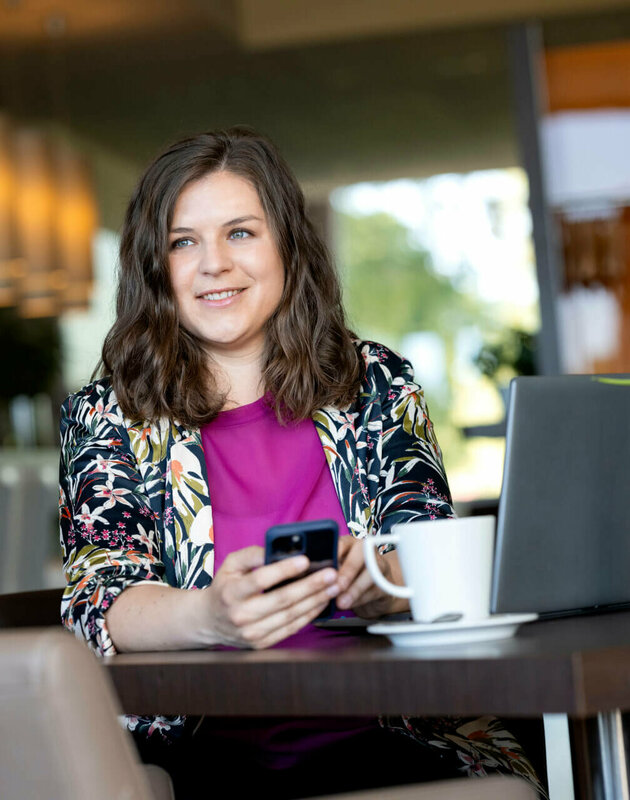 Viktoria Rathjen sitzt an einem Tisch im Restaurant mit Handy in der Hand, Laptop vor der Nase und einem Kaffee