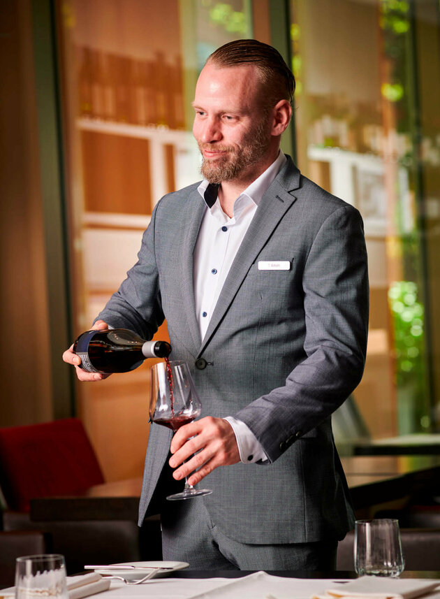 Tobias Wilhelm schenkt ein Glas Rotwein am Tisch ein.